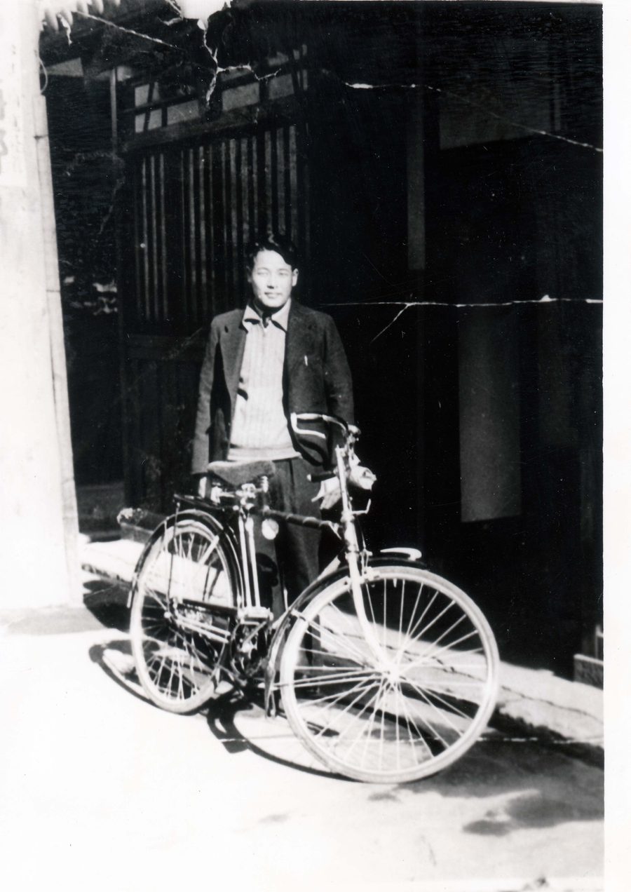 Kunio Kaneda with his bicycle in front of a Japanese wooden house